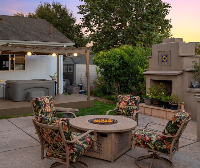 patio terrace at dusk with an outdoor fire pit, a storage unit, an outbuilding, and an outdoor fireplace