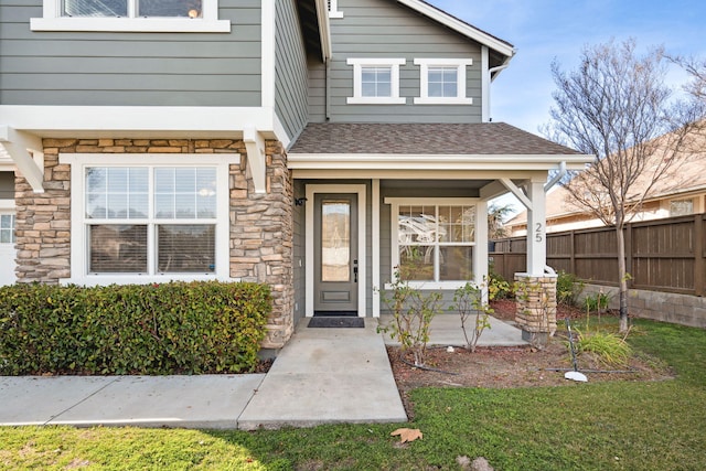 property entrance featuring a shingled roof, stone siding, and fence