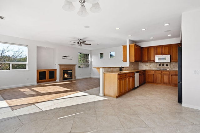 kitchen featuring brown cabinetry, white microwave, open floor plan, a peninsula, and light countertops