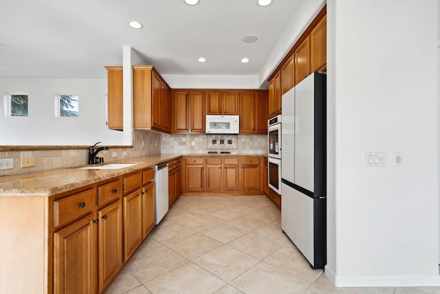 kitchen featuring brown cabinetry, a sink, light stone countertops, stainless steel appliances, and backsplash