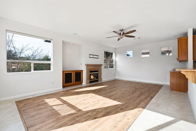 unfurnished living room with light wood finished floors, baseboards, a ceiling fan, and a glass covered fireplace