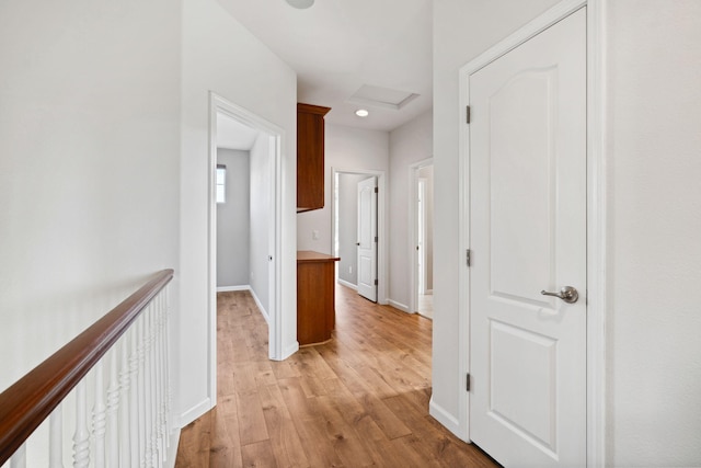 corridor featuring light wood-type flooring, attic access, and baseboards