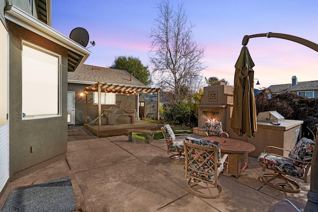 patio terrace at dusk with a lit fireplace, a pergola, and area for grilling