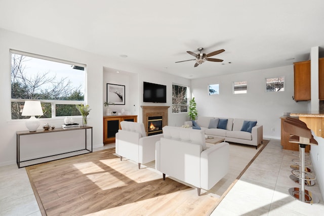 living room featuring light wood-type flooring, ceiling fan, baseboards, and a glass covered fireplace