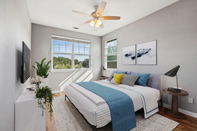 bedroom with ceiling fan, wood finished floors, visible vents, and baseboards