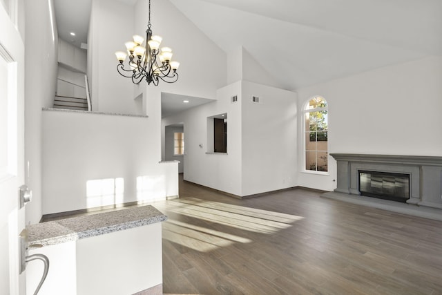 unfurnished living room featuring dark wood-type flooring, high vaulted ceiling, and a notable chandelier