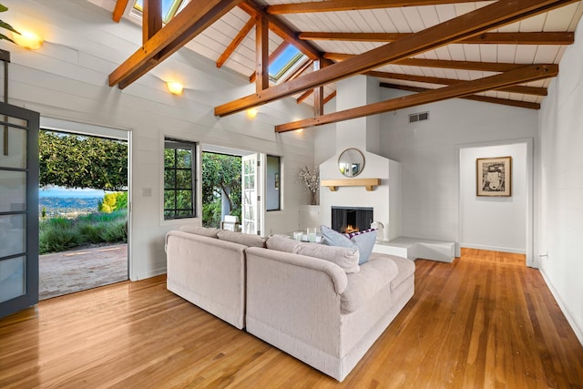 living room with a large fireplace, light wood-type flooring, beam ceiling, and high vaulted ceiling