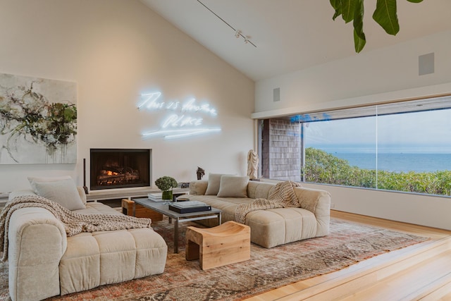 living room featuring hardwood / wood-style floors, track lighting, high vaulted ceiling, and a water view