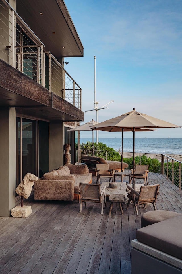 wooden deck featuring outdoor lounge area, a water view, and a view of the beach