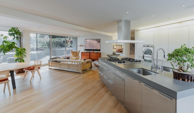 kitchen featuring island exhaust hood, light hardwood / wood-style floors, sink, gray cabinets, and stainless steel gas stovetop