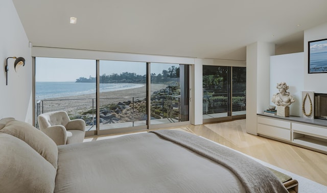 bedroom with access to exterior, light wood-type flooring, a water view, a wall of windows, and a beach view