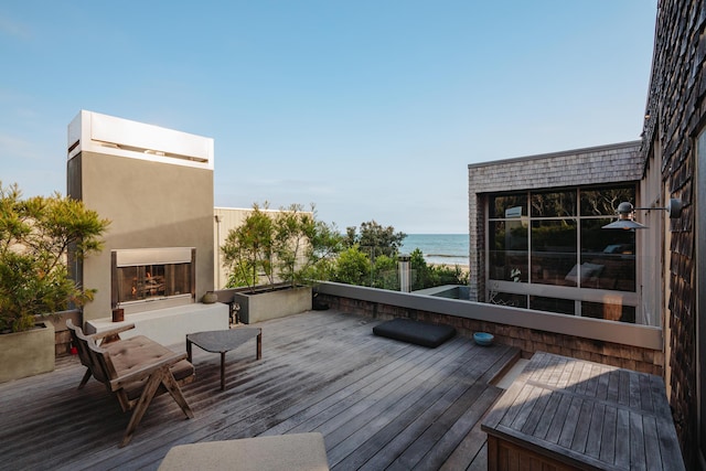 wooden terrace with a water view and an outdoor fireplace