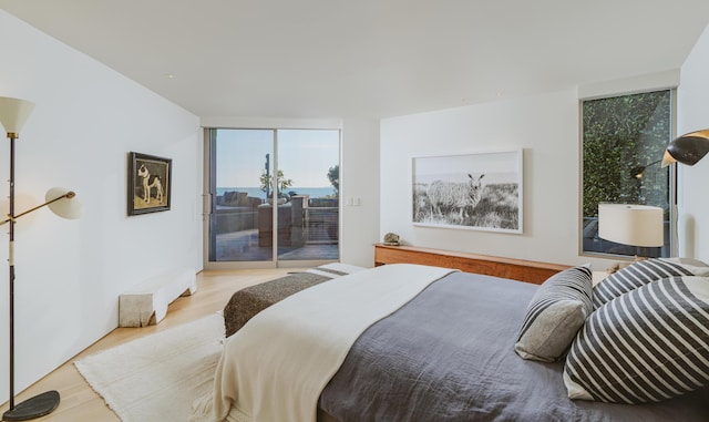 bedroom with access to exterior, light wood-type flooring, and floor to ceiling windows