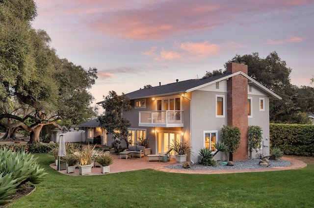 back house at dusk with a yard, outdoor lounge area, a balcony, and a patio