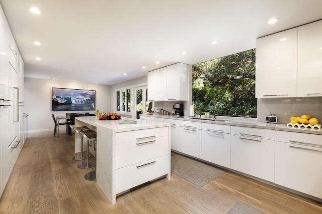 kitchen featuring a kitchen breakfast bar, sink, a center island, light hardwood / wood-style floors, and white cabinetry