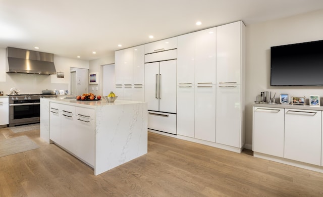 kitchen with a center island, wall chimney exhaust hood, light wood-type flooring, premium appliances, and white cabinetry