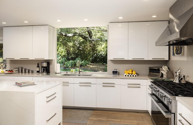 kitchen featuring sink, stainless steel stove, light hardwood / wood-style floors, white cabinetry, and extractor fan