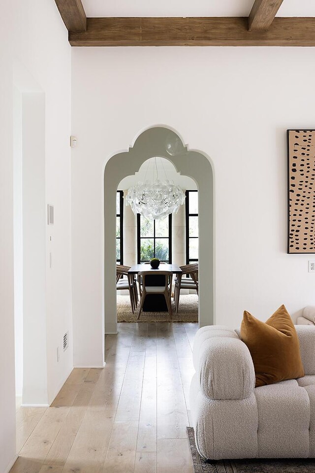 hall featuring beam ceiling, light wood-type flooring, and a chandelier