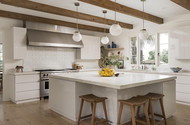 kitchen featuring a center island, stainless steel stove, decorative light fixtures, white cabinets, and exhaust hood