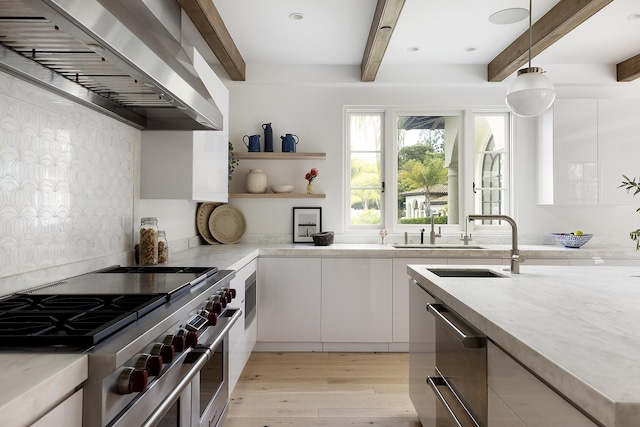 kitchen featuring appliances with stainless steel finishes, wall chimney range hood, beamed ceiling, white cabinets, and hanging light fixtures