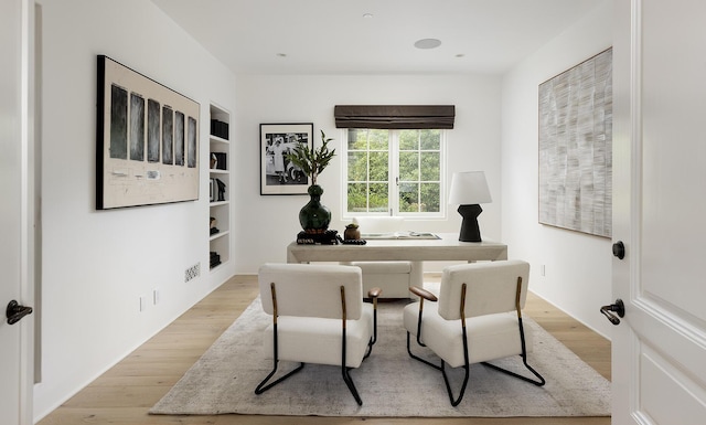 home office with built in shelves and light hardwood / wood-style floors