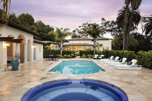 pool at dusk featuring a patio area and an in ground hot tub