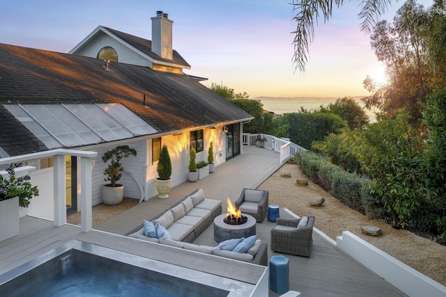 patio terrace at dusk featuring a deck with water view and an outdoor living space with a fire pit