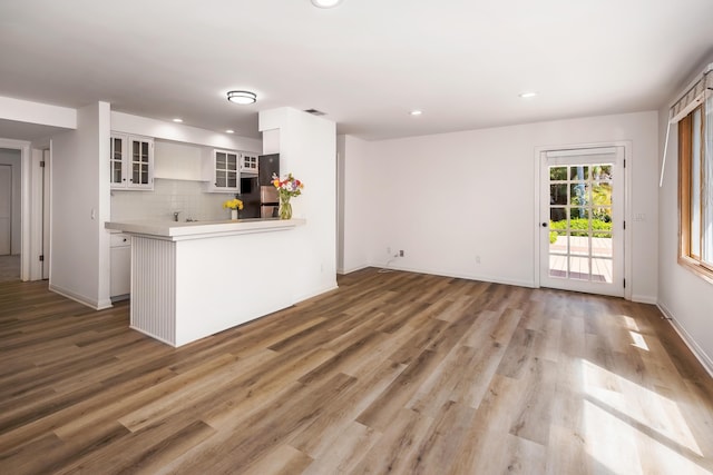 kitchen featuring kitchen peninsula, stainless steel fridge, backsplash, wood-type flooring, and white cabinets