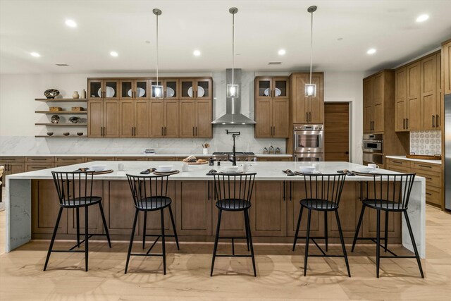 kitchen with glass insert cabinets, a spacious island, light countertops, and wall chimney exhaust hood