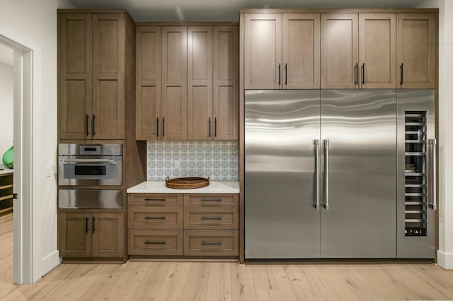 kitchen with a warming drawer, tasteful backsplash, light countertops, light wood-style flooring, and appliances with stainless steel finishes