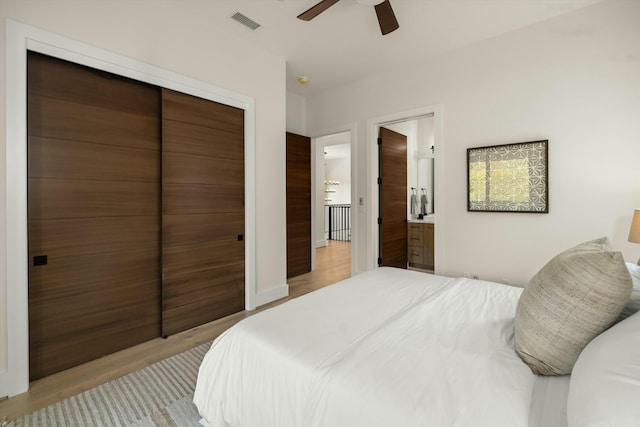 bedroom featuring ceiling fan, ensuite bathroom, visible vents, a closet, and light wood-type flooring