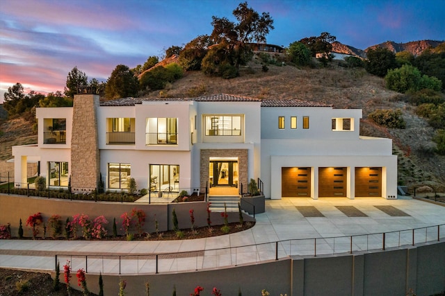 rear view of house with concrete driveway, a chimney, fence, and stucco siding