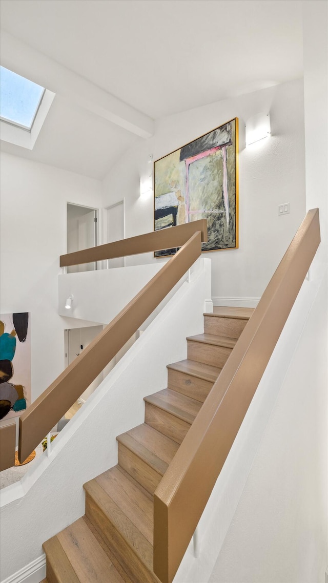 stairs featuring wood-type flooring and vaulted ceiling with skylight