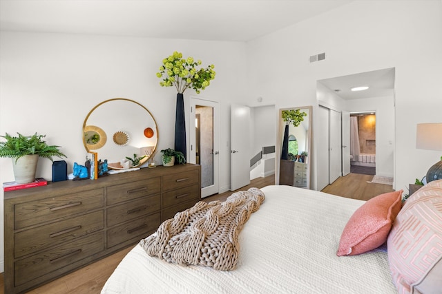 bedroom with ensuite bath, a closet, light hardwood / wood-style flooring, and a high ceiling