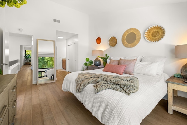 bedroom with hardwood / wood-style floors, a towering ceiling, and connected bathroom