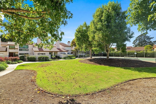 view of property's community with a lawn and tennis court