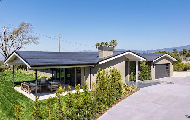 exterior space featuring concrete driveway, a front lawn, a mountain view, an outdoor hangout area, and stucco siding