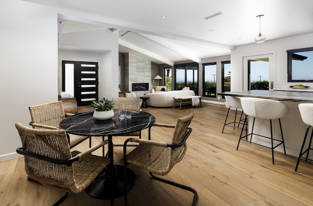 dining room featuring vaulted ceiling with beams, a large fireplace, light wood-style flooring, baseboards, and visible vents