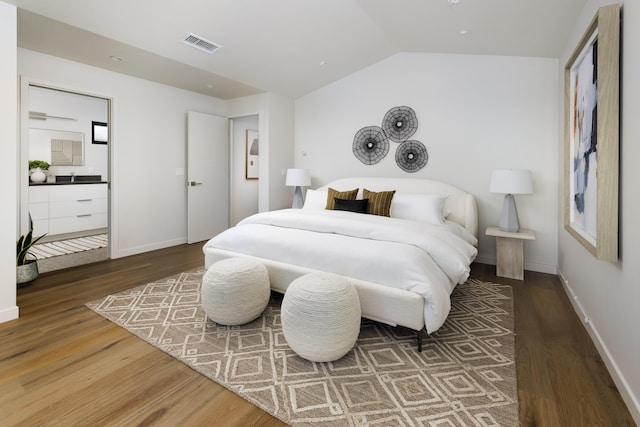 bedroom featuring lofted ceiling, wood finished floors, visible vents, ensuite bath, and baseboards