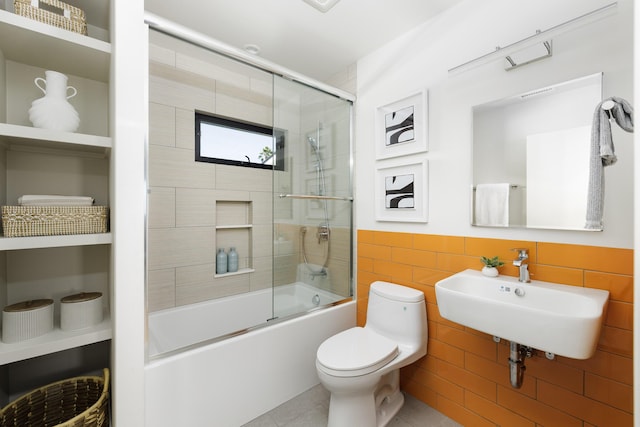 full bathroom with a wainscoted wall, combined bath / shower with glass door, toilet, a sink, and tile walls