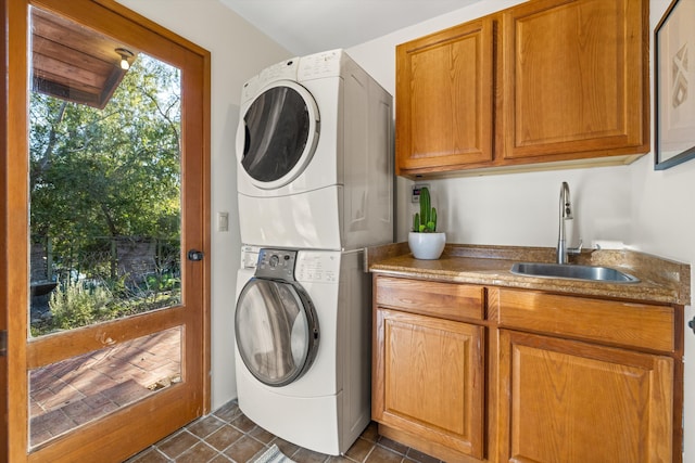 clothes washing area featuring stacked washer / drying machine, cabinets, dark tile patterned floors, and sink