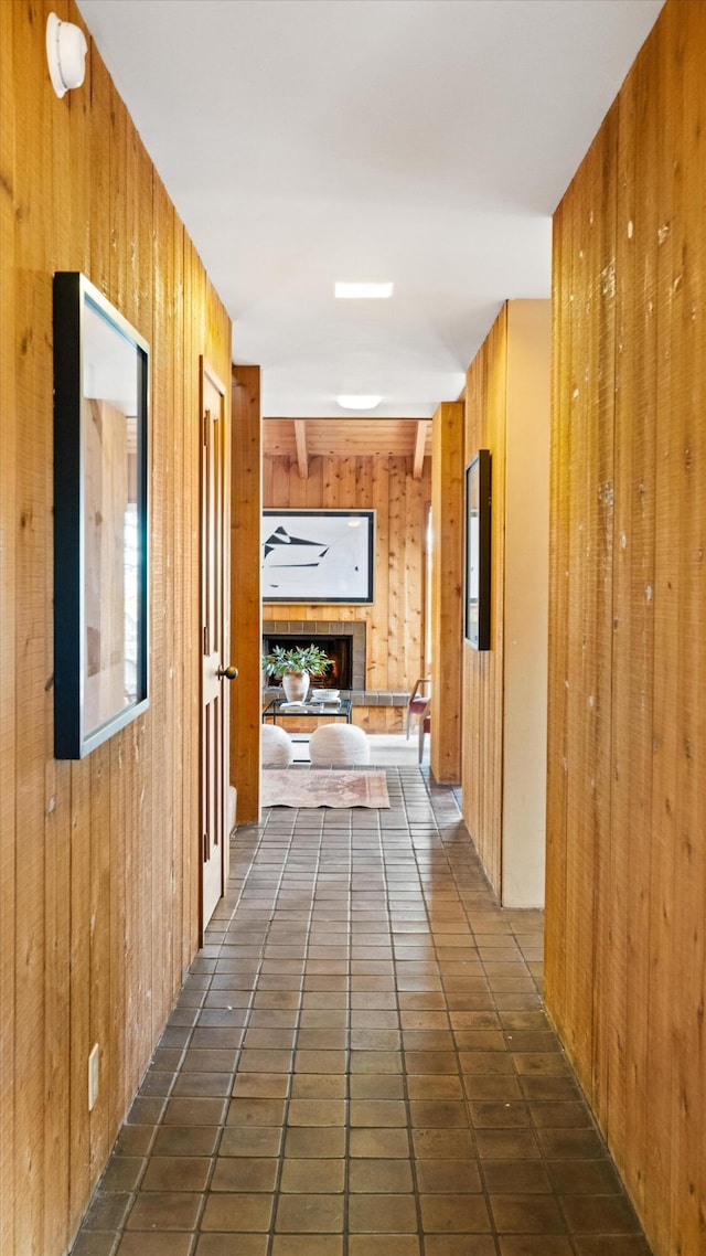 hallway featuring beamed ceiling, wooden walls, and dark tile patterned flooring