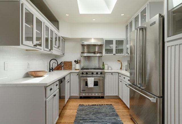 kitchen with premium appliances, decorative backsplash, wall chimney range hood, and light hardwood / wood-style flooring