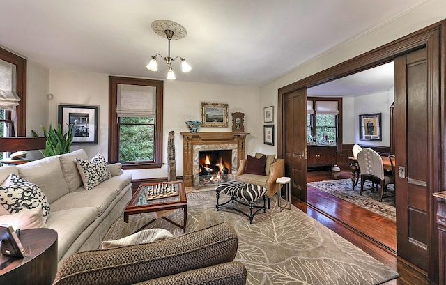 living room with dark wood-type flooring, a high end fireplace, a wealth of natural light, and a chandelier