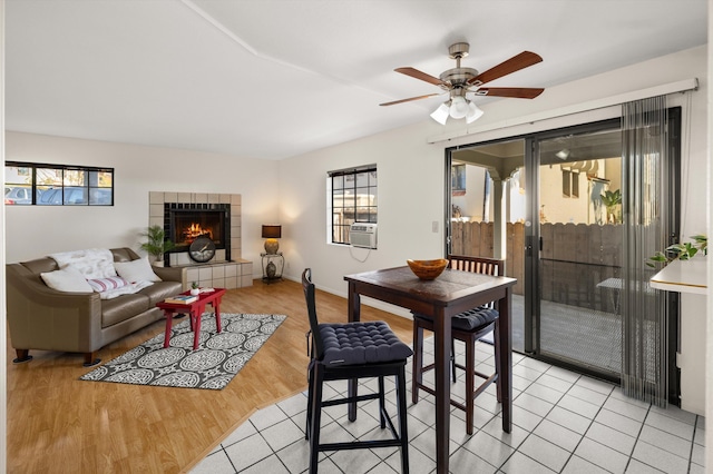 dining area featuring a tile fireplace, ceiling fan, light hardwood / wood-style flooring, and cooling unit