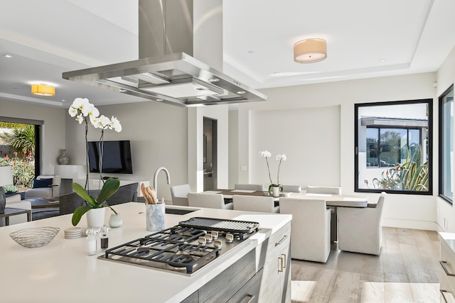 kitchen featuring light wood-type flooring, island range hood, stainless steel gas cooktop, and sink