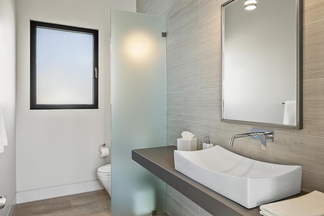 bathroom with hardwood / wood-style flooring, toilet, sink, and tile walls