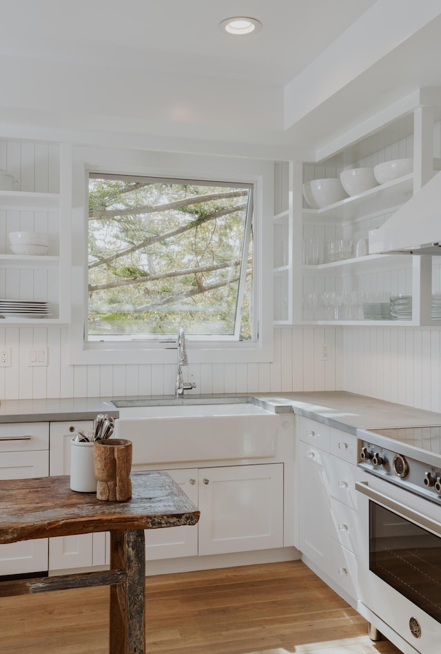 kitchen with sink, white cabinetry, range, light wood-type flooring, and wall chimney range hood