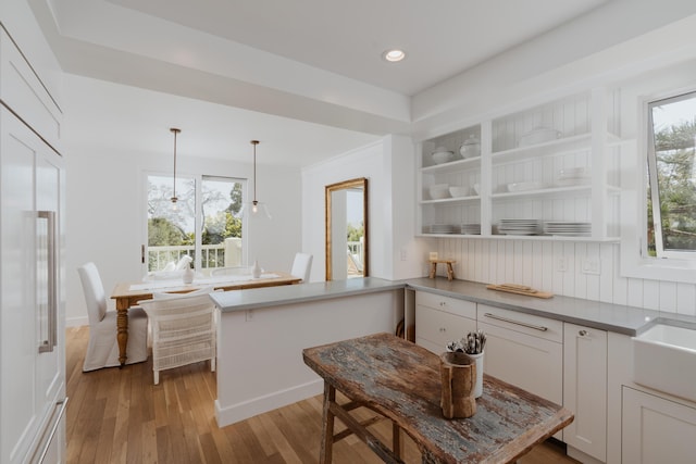 kitchen featuring white cabinetry, decorative light fixtures, kitchen peninsula, and light wood-type flooring