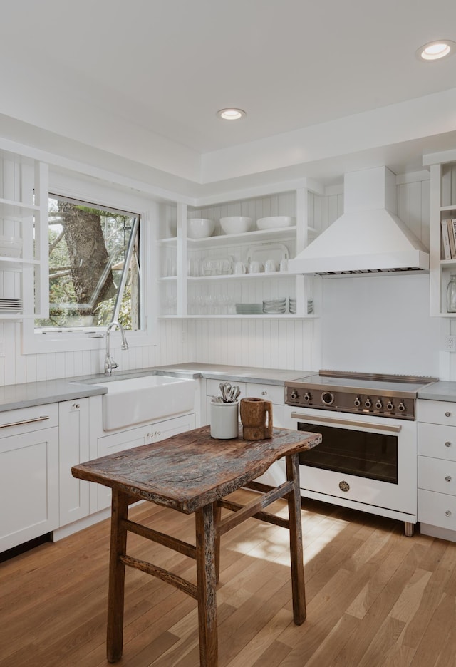 kitchen with high end white range, sink, white cabinets, custom exhaust hood, and light wood-type flooring